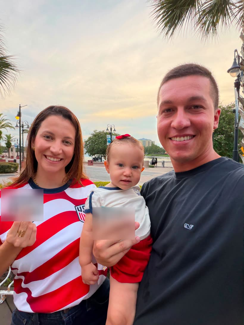 Casal com o bebê no colo à beira-mar, vestindo camisas dos Estados Unidos